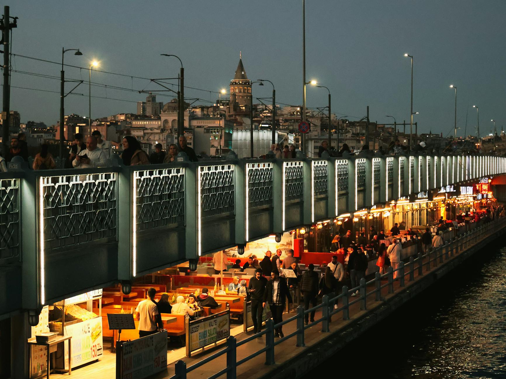 夜の明かりが灯るガラタ橋を散策する、人々とレストラン。