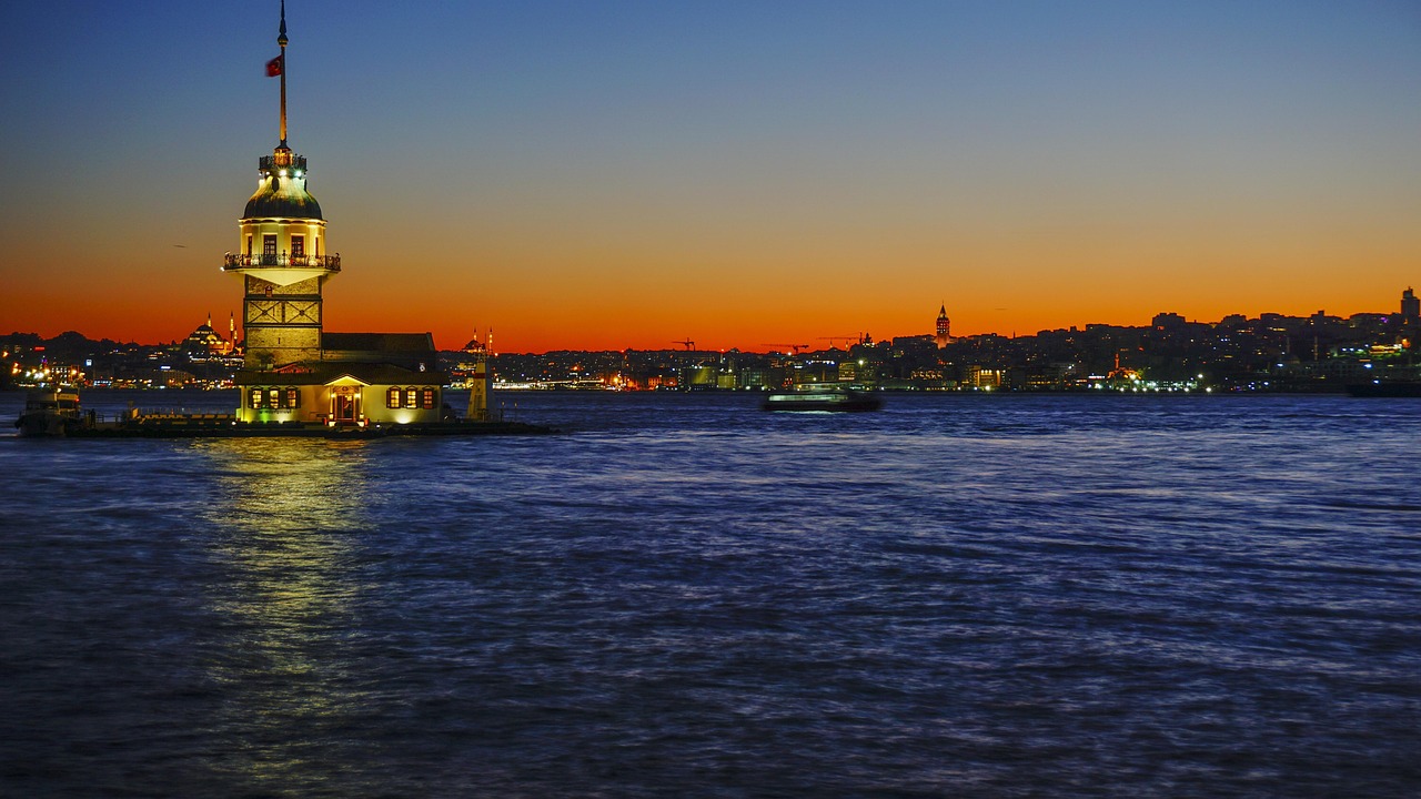 黄昏時の海に輝く乙女の塔と遠くに広がる街の灯り。